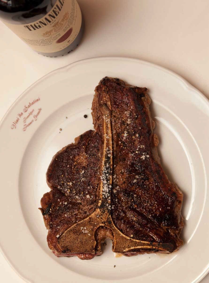 T-Bone-Steak auf dem Teller, dahinter eine Flasche Tignanello