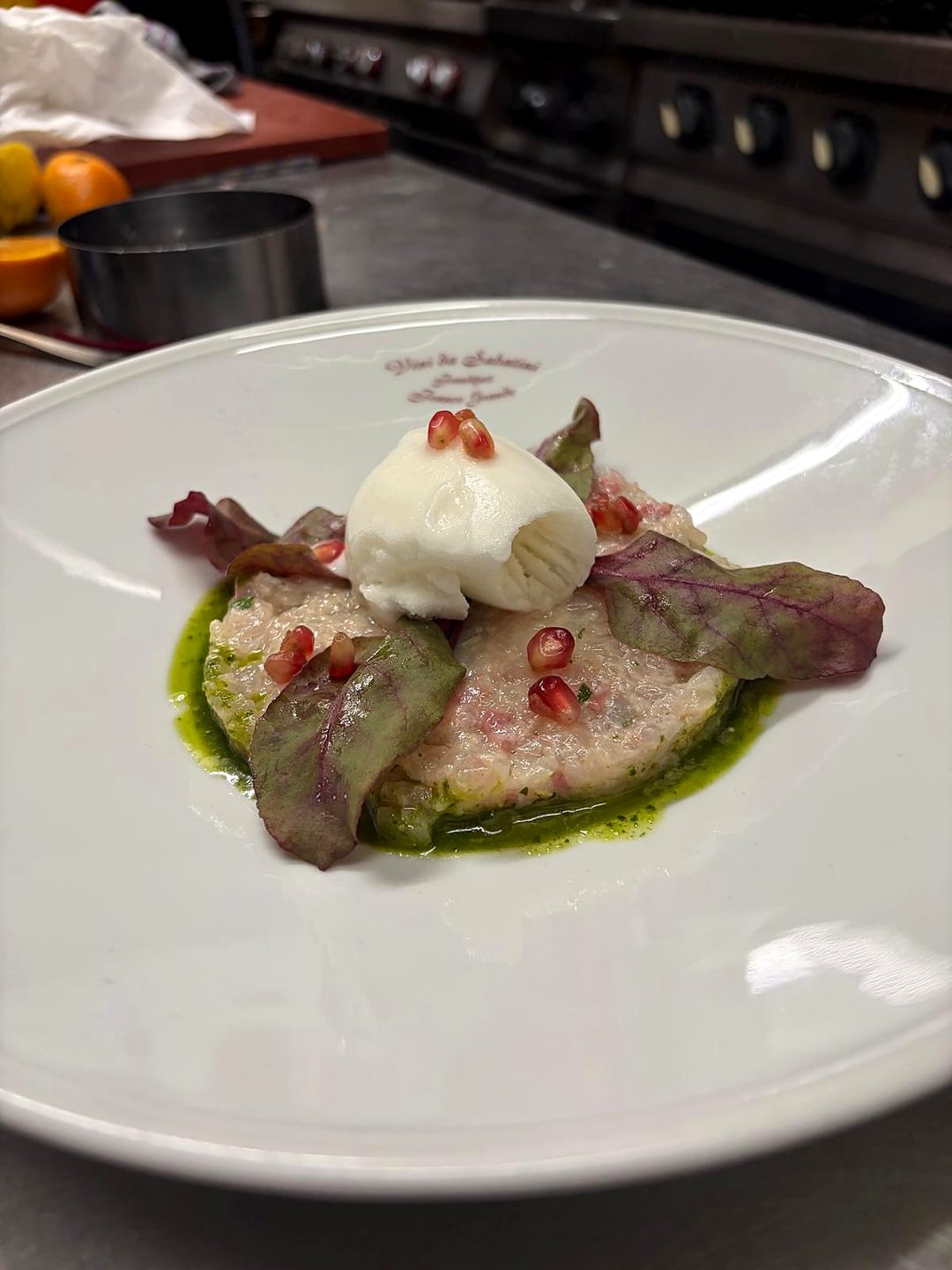 Tatar mit Burrata, Granatapfel und Kräuteröl auf einem Teller mit dem Schriftzug des Hauses